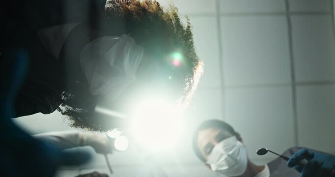 Face, people and dentist with tools for surgery with lights, cleaning and teeth whitening for hygiene. Pov, employees and inspection with tooth extraction, root canal and dental implant and procedure