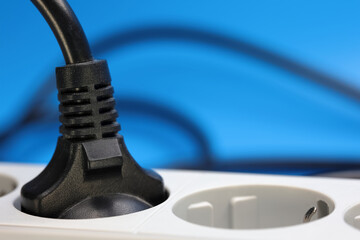 A Detailed View Of A Black Power Plug Connected To A White Electrical Socket. The Background Is A Vibrant Blue, Emphasizing The Contrast And Focus On Energy And Connectivity.