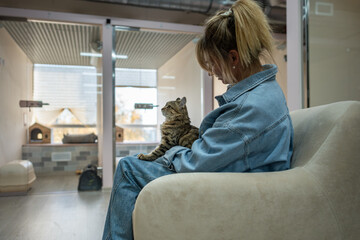 Woman worker holds cat on lap, gently petting and talking, assisting in adjusting to unfamiliar...