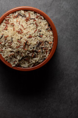 Earthenware bowl full of long, red, wild rice on a kitchen countertop in a zenithal photograph
