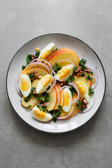 Fresh salad with apples, sorrel, red onion, boiled eggs and walnuts on a gray plate on a concrete background. Seasonal recipe of healthy salad