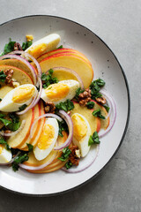 Fresh salad with apples, sorrel, red onion, boiled eggs and walnuts on a gray plate on a concrete background. Seasonal recipe of healthy salad