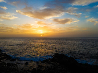 Atlantic ocean sunset in Tenerife with soft golden hues illuminating the horizon, waves gently crashing against the rocky shore.  A scene that evokes a sense of tranquility and connection with nature