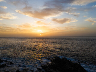 Atlantic ocean sunset in Tenerife with soft golden hues illuminating the horizon, waves gently crashing against the rocky shore.  A scene that evokes a sense of tranquility and connection with nature