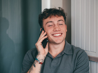 Young happy caucasian man while talking on his smartphone sitting in outdoor enjoying tech and social