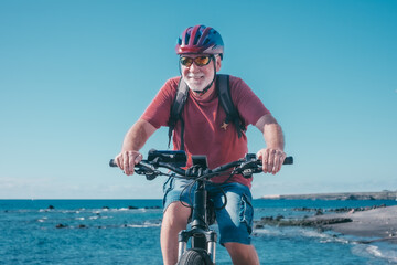 Portrait of active senior man with helmet enjoying riding bike at sea to be fit and healthy....
