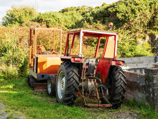 Obraz premium Old small tractor and excavator parked by a fence in a rural area. Working on a farm concept.