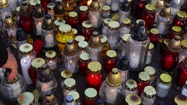 Many glass candles burning on a grave. Panning from lest to right in natural daylight.