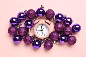 Alarm clock with Christmas balls on pink background