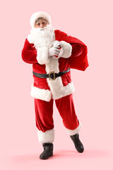 Santa Claus with bag full of Christmas gifts on pink background