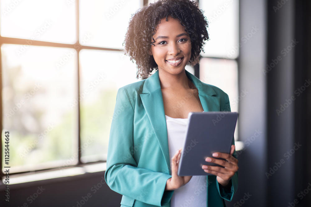 Leinwandbilder A diverse team member stands in a modern office, smiling and using a tablet. Sunlight streams through large windows, creating a warm atmosphere ideal for collaboration and success.