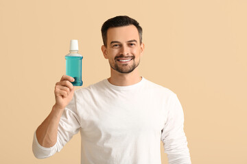 Handsome man with mouth rinse on beige background