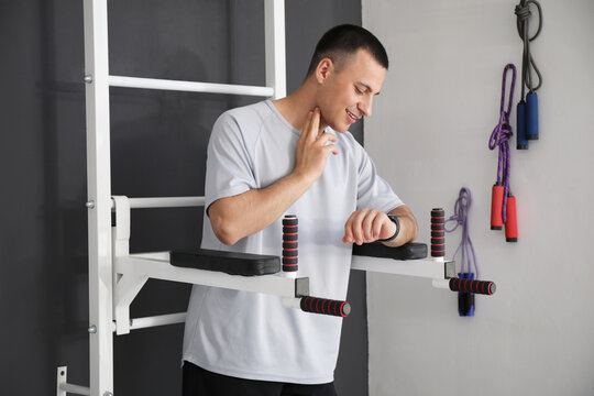 Sporty young man with smartwatch checking pulse near wall bars in gym - Powered by Adobe