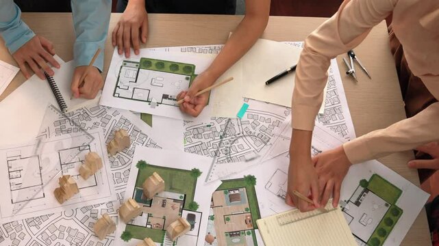 Architect and safety engineer discussion about building construction use blueprint on table with architectural document, measurement tool and wooden block scatter around at modern office. Delineation.