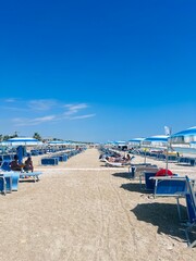 Sunny beach with blue umbrellas and sun loungers in summer. Porto Sant'Elpidio, Italy.
