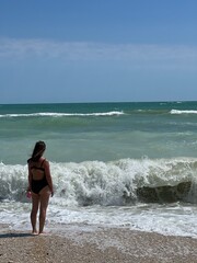 Woman standing at the beach gazing at ocean waves under clear sky