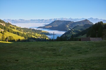 A serene view from the slopes of Mount Rigi, Switzerland, showcasing green valleys, a wooden cross,...