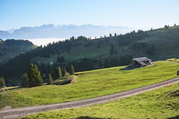 A rural scene on the slopes of Mount Rigi, Switzerland. Distant Alpine peaks rise under a clear...