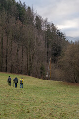 Three male hikers are descending a mountainside near a forest.

