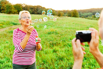 woman man outdoor senior couple happy fun retirement together bubble soap camera taking pictures...