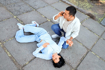 Young man calling ambulance for his wife having heart attack on street