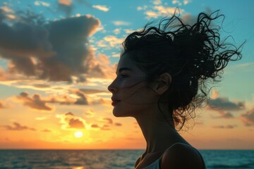 Fototapeta premium A woman stands alone on a beach at sunset, looking out at the vast ocean