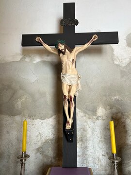 Cruxifixo colonial antigo de arte sacra entre dois cancelabros com velas amarelas 