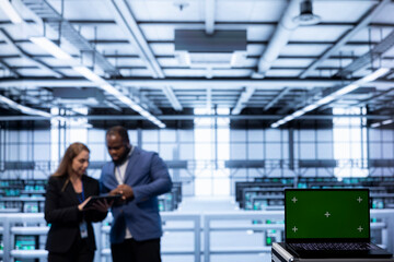 Focus on isolated screen laptop device used by coworkers in data center blurry background. Close up of Chroma key notebook in server hub optimizing data center infrastructure