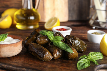 Cutting board with tasty Dolmas (stuffed grape leaves), sour cream and spices on wooden table