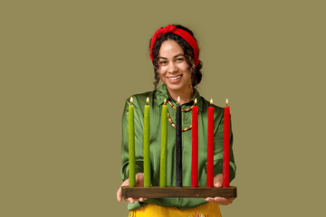Young African-American woman with burning candles on green background. Kwanzaa celebration
