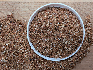 Buckwheat Grains on the white plate on wooden kitchen board. Top view
