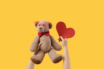 Woman holding toy bear with heart on yellow background. Valentine's Day celebration