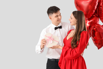 Young couple in love with gift box and balloons on light background. Valentine's Day celebration