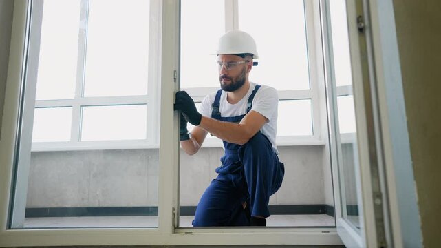 Construction worker in protective gear uses a power drill to secure a window frame in place