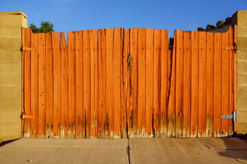 Fototapeta premium Driveway entrance gate with well weathered painted in red wooden planks and metal handle in between block columns