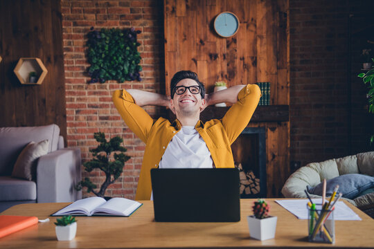 Young man enjoying leisure time indoors, smiling and relaxing at home office desk with hands behind head, casual lifestyle