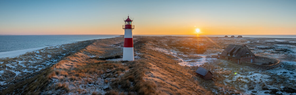 Red and white striped lighthouse situated on a coastal landscape at sunrise in winter. Lighthouse West-List on the Ellenbogen (the "Elbow"), the peninsula on northern coast of Sylt island in winter