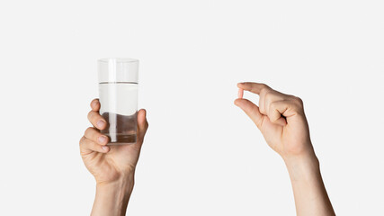 Cropped view of millennial guy holding glass of water and pill on light background, closeup. Panorama