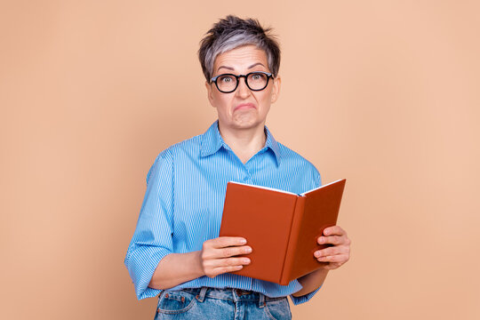 Elderly woman with a quirky expression holding a book against a beige background, wearing a stylish striped shirt