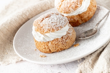 Cream puffs, semla, pastry from choux covered sugar powder on white plate over stone table background. Sweet dessert with chantilly cream