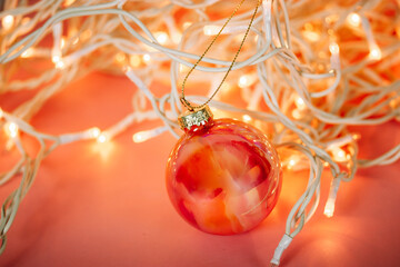 Orange glass ball, Christmas toy among tangled white wires of garland lights. New Year 2024 decor...