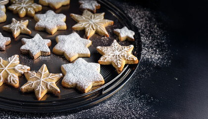 Freshly baked Christmas cookies shaped like stars and snowflakes on a decorative tray topped with powdered sugar