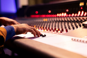 Audio expert recording and editing music with mixing console panel board, twisting knobs and...