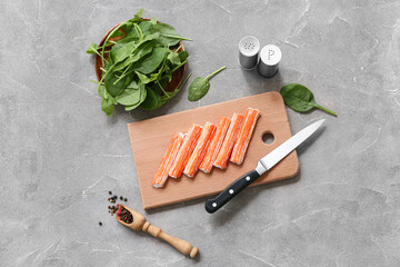 Wooden board with tasty crab sticks and spinach leaves on grey background © Pixel-Shot