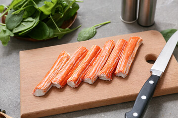 Wooden board with tasty crab sticks and spinach leaves on grey background © Pixel-Shot