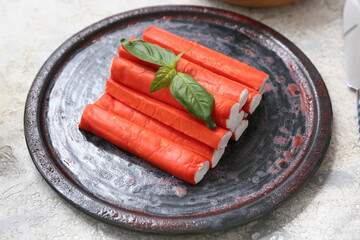 Plate with tasty crab sticks and basil leaves on white background © Pixel-Shot