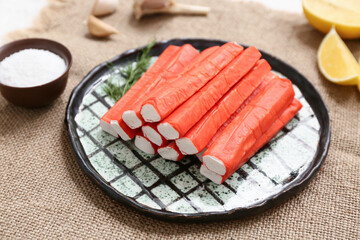 Plate with tasty crab sticks, dill and bowl of salt on sack cloth background © Pixel-Shot