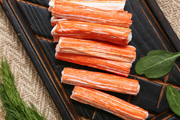 Wooden board with tasty crab sticks, spinach leaves and dill on sack cloth background, closeup © Pixel-Shot