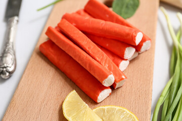 Wooden board with tasty crab sticks, slices of lemon and green onion on grey background, closeup © Pixel-Shot