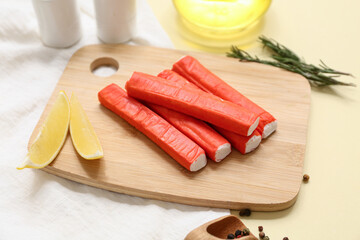 Wooden board with tasty crab sticks, slices of lemon and rosemary on yellow background © Pixel-Shot